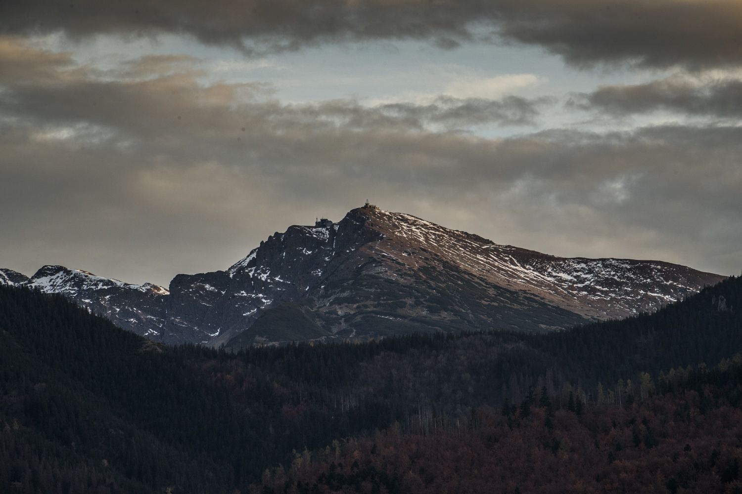A mountain with snow-capped peaks and a forested valley.