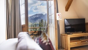 Quarto com uma janela ampla que oferece vista para as montanhas, um rack de TV de madeira e uma cama aconchegante com travesseiro.