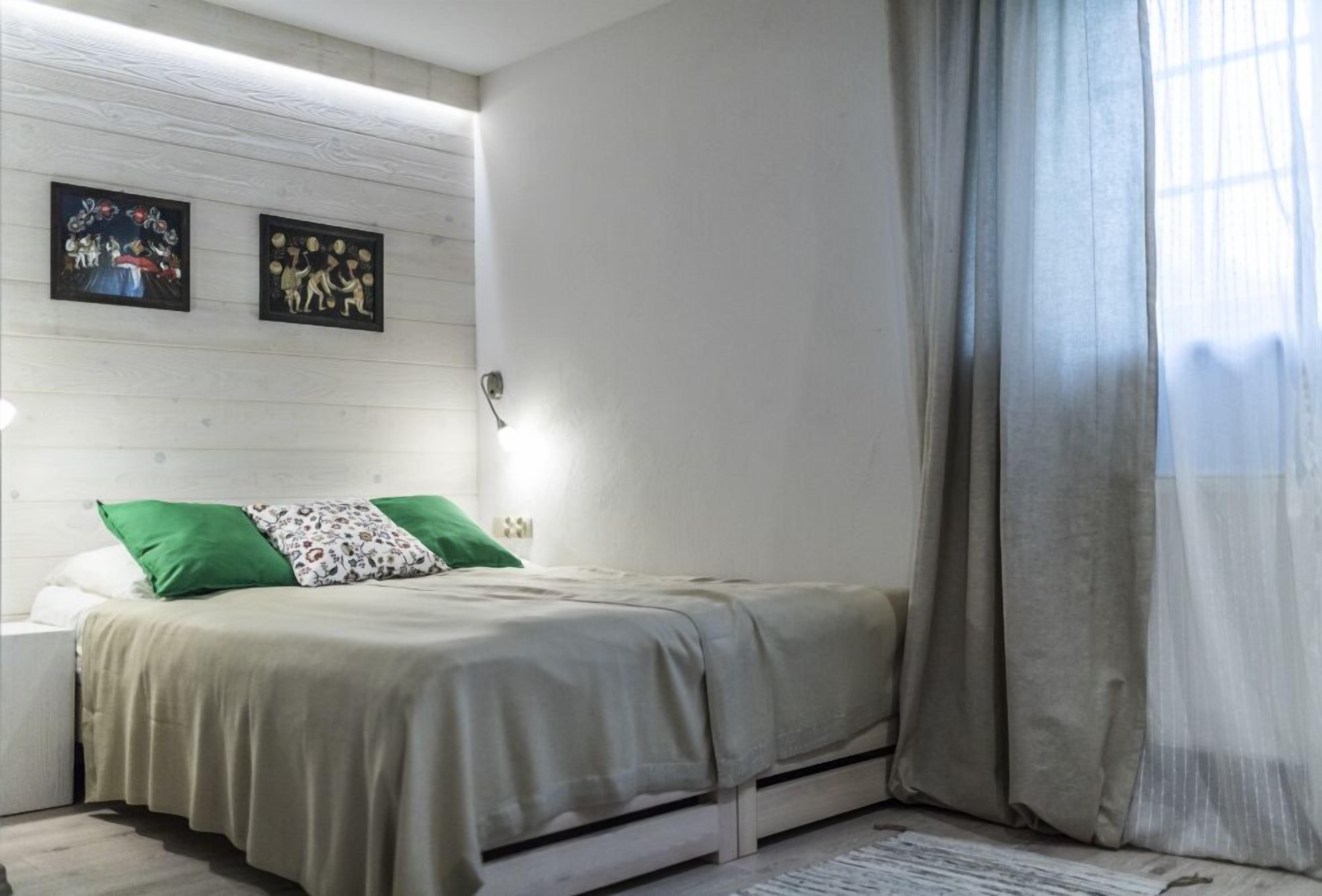 A bedroom with a bed, green and white pillows, a nightstand, and two wall-mounted artworks.