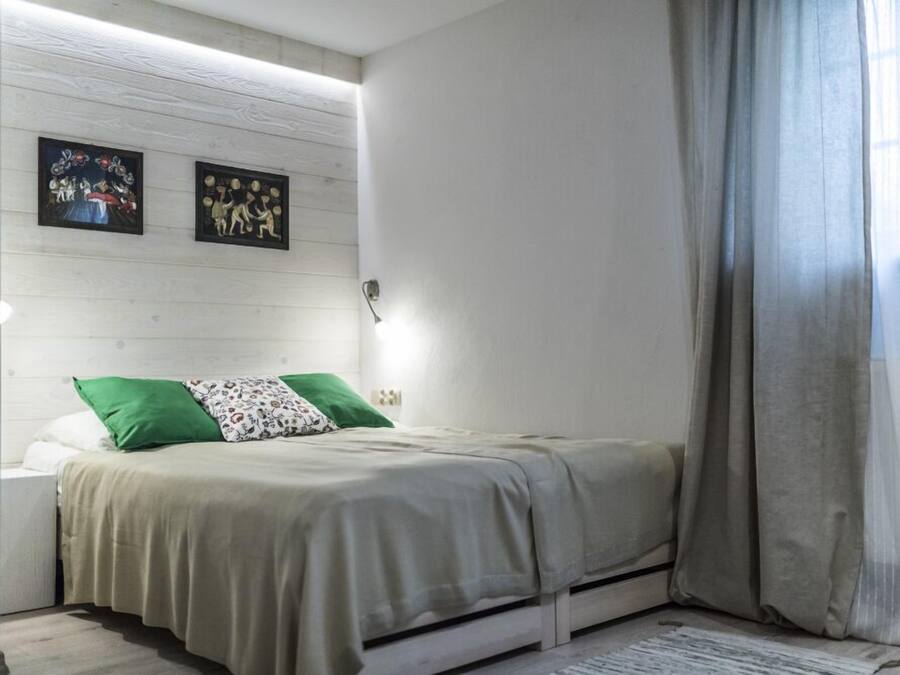 A bedroom with a bed, green and white pillows, a nightstand, and two wall-mounted artworks.