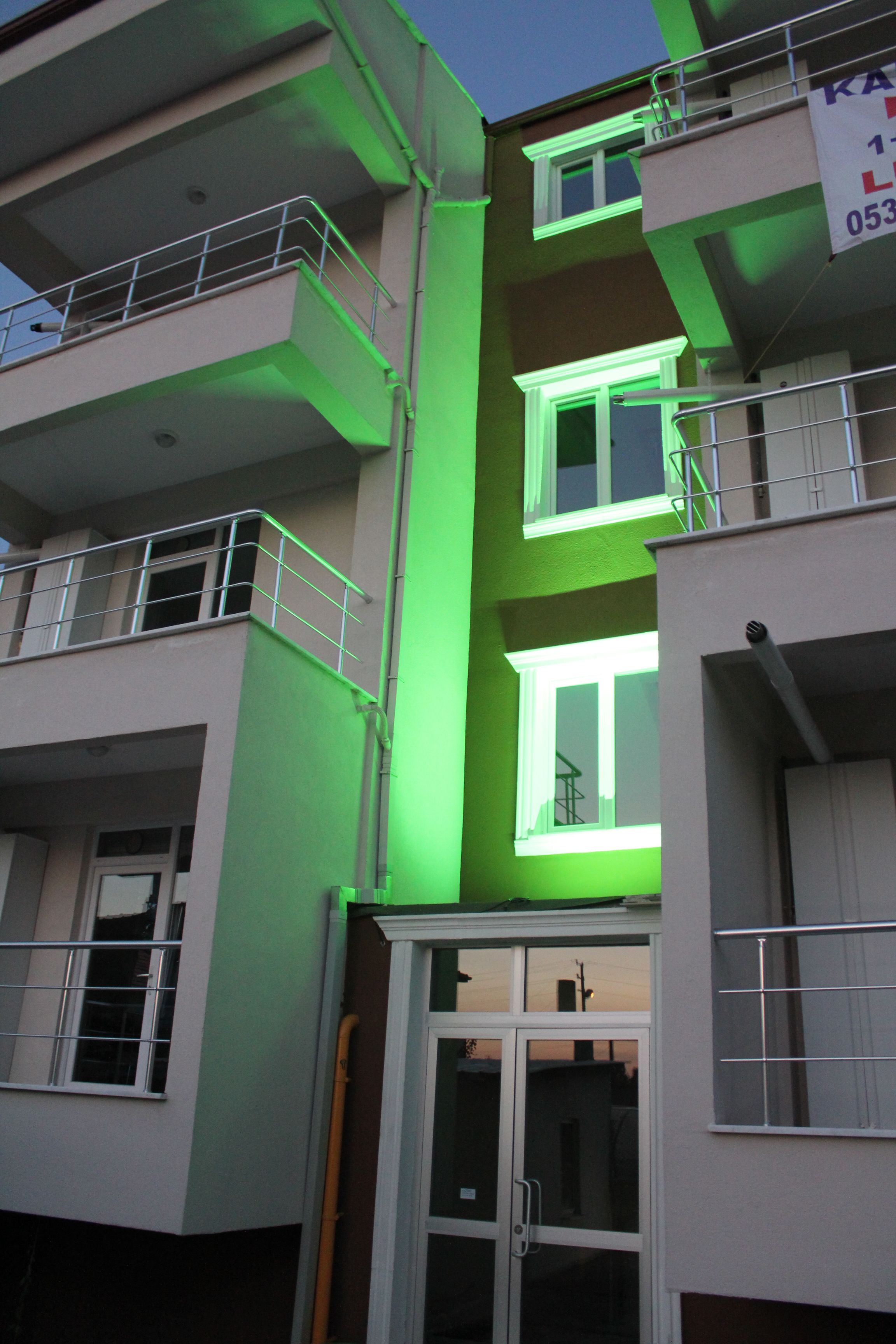 Un immeuble à plusieurs étages, doté de balcons et d’une entrée illuminée de lumière verte.