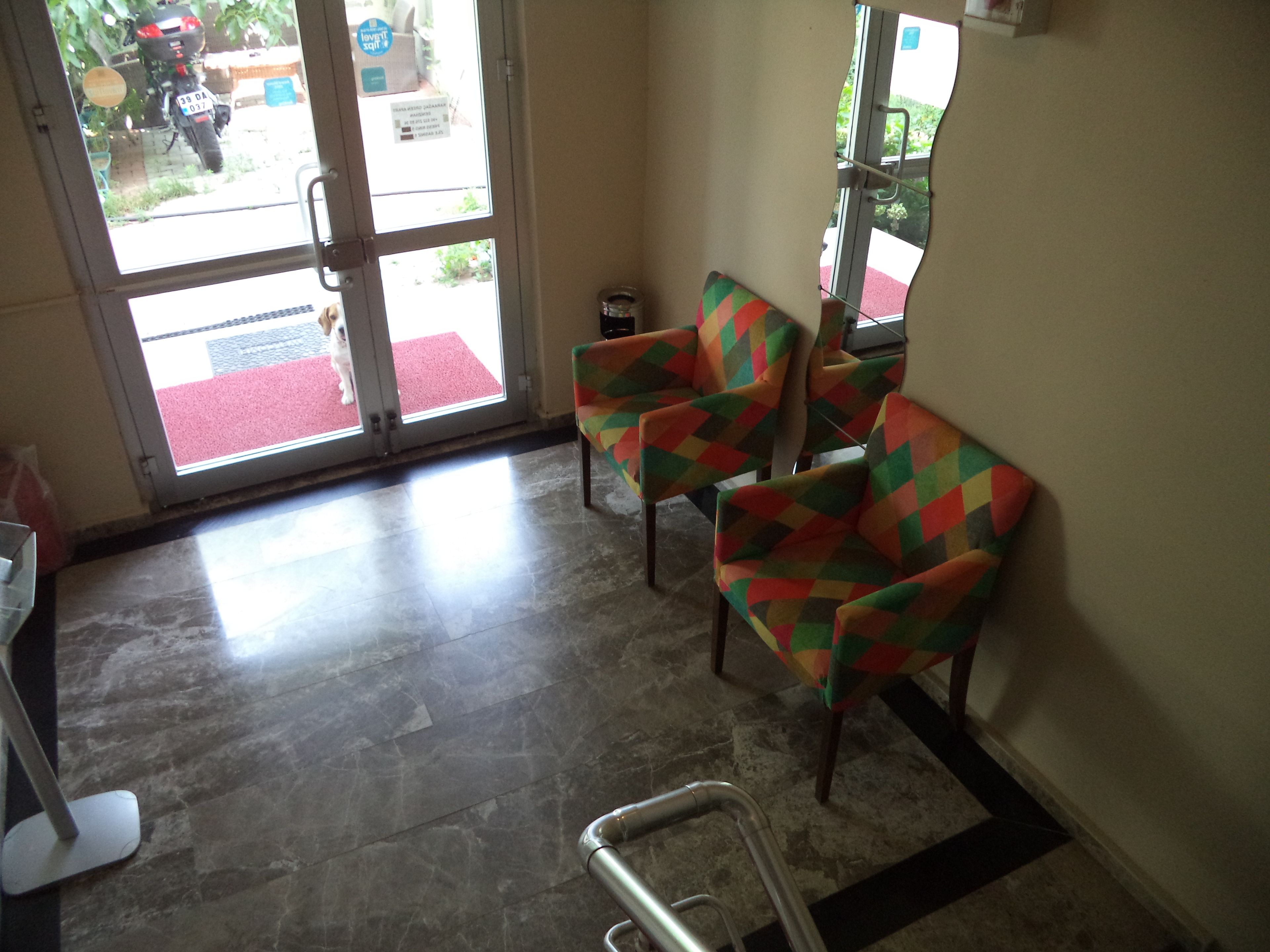 Un área de recepción con suelo de baldosas, una silla de ruedas y sillas de colores.