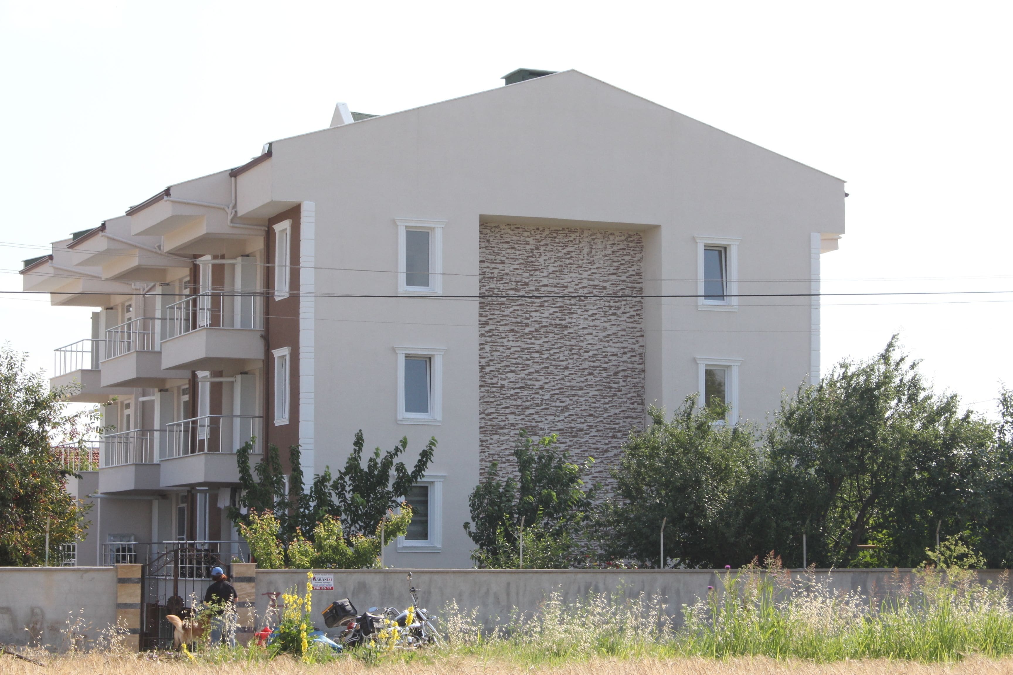 A multi-story residential building with balconies, a stone facade, and a surrounding grassy area.