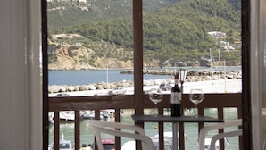 A view from a balcony overlooking a marina with boats, a rocky shoreline, and buildings on a hillside. - Georgios L (Skopelos)