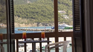 A view from a balcony overlooking a coastal area with boats, a rocky shoreline, and buildings in the background. - Georgios L (Skopelos)