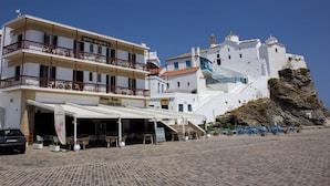 A hotel with multiple floors, outdoor seating, and a view of a white building with a tower. - Georgios L (Skopelos)