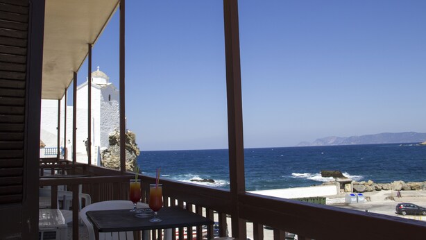 A seaside restaurant with a view of the ocean and a white building in the background. - Georgios L (Skopelos)
