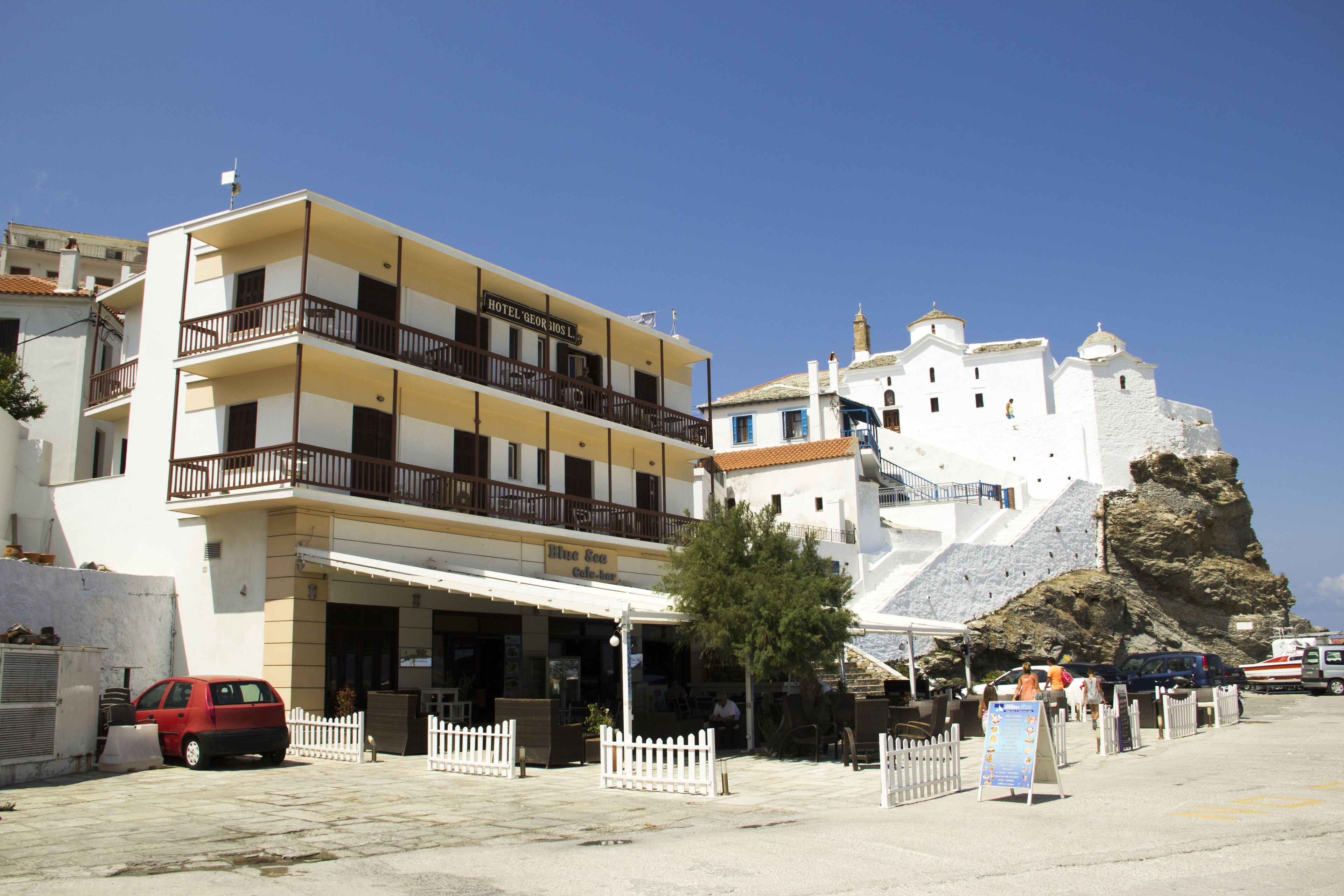 A hotel with a balcony, a white fence, and a rocky cliff in the background.