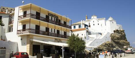 A hotel with a balcony, a white fence, and a rocky cliff in the background.