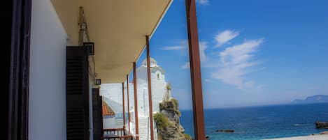 Un balcón con vista al mar, un edificio blanco con una torre de campanas y un camino de piedra.