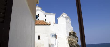 A coastal building with white walls and a red-tiled roof, overlooking the sea.