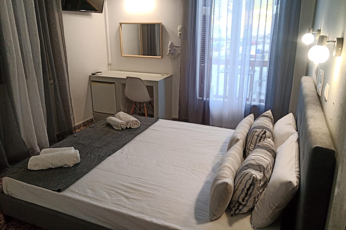 A hotel room with a bed, a desk, a chair, a TV, and a window with curtains.