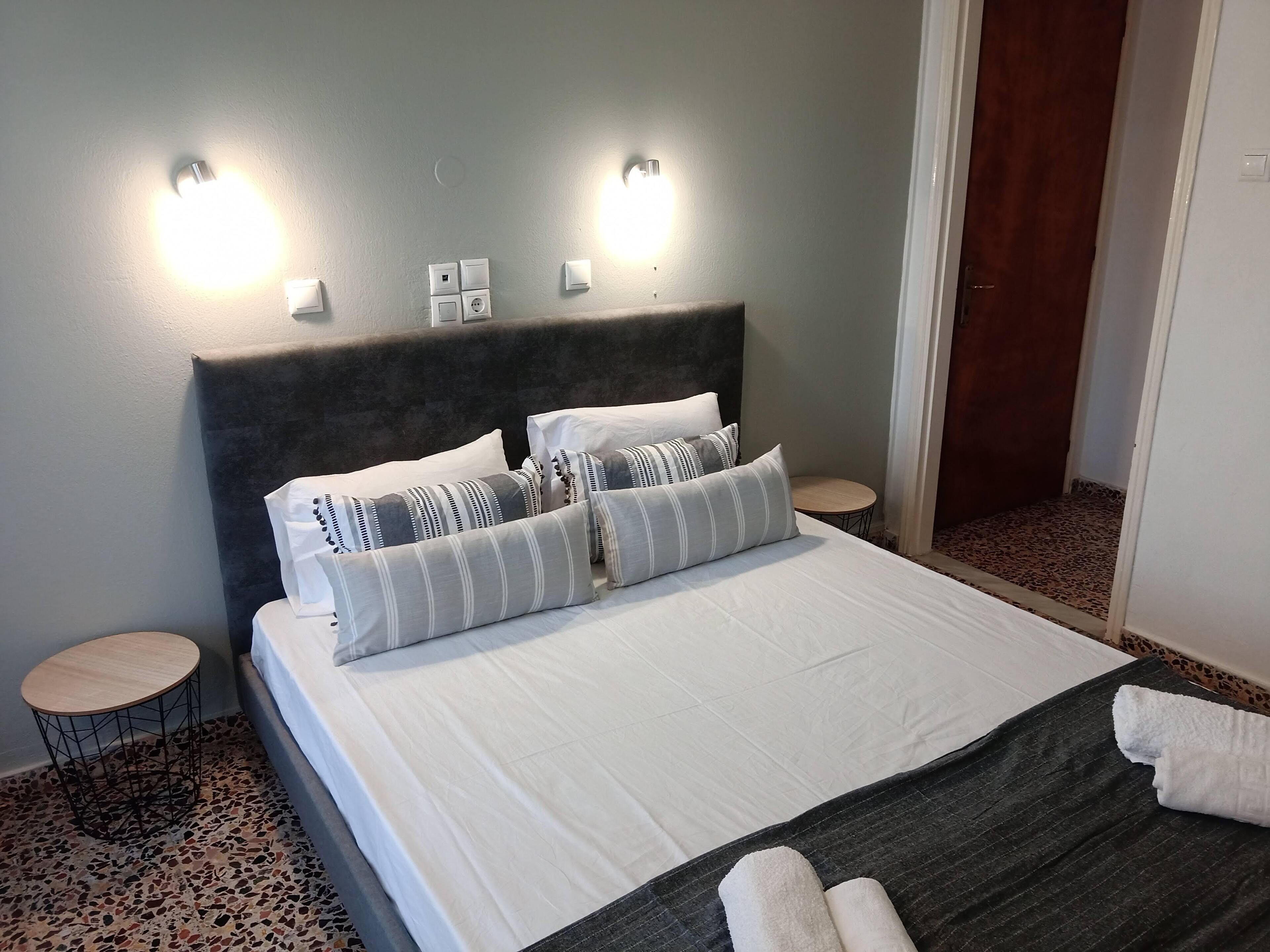 A neatly made bed with white and striped pillows, a dark headboard, and two bedside tables with lamps.