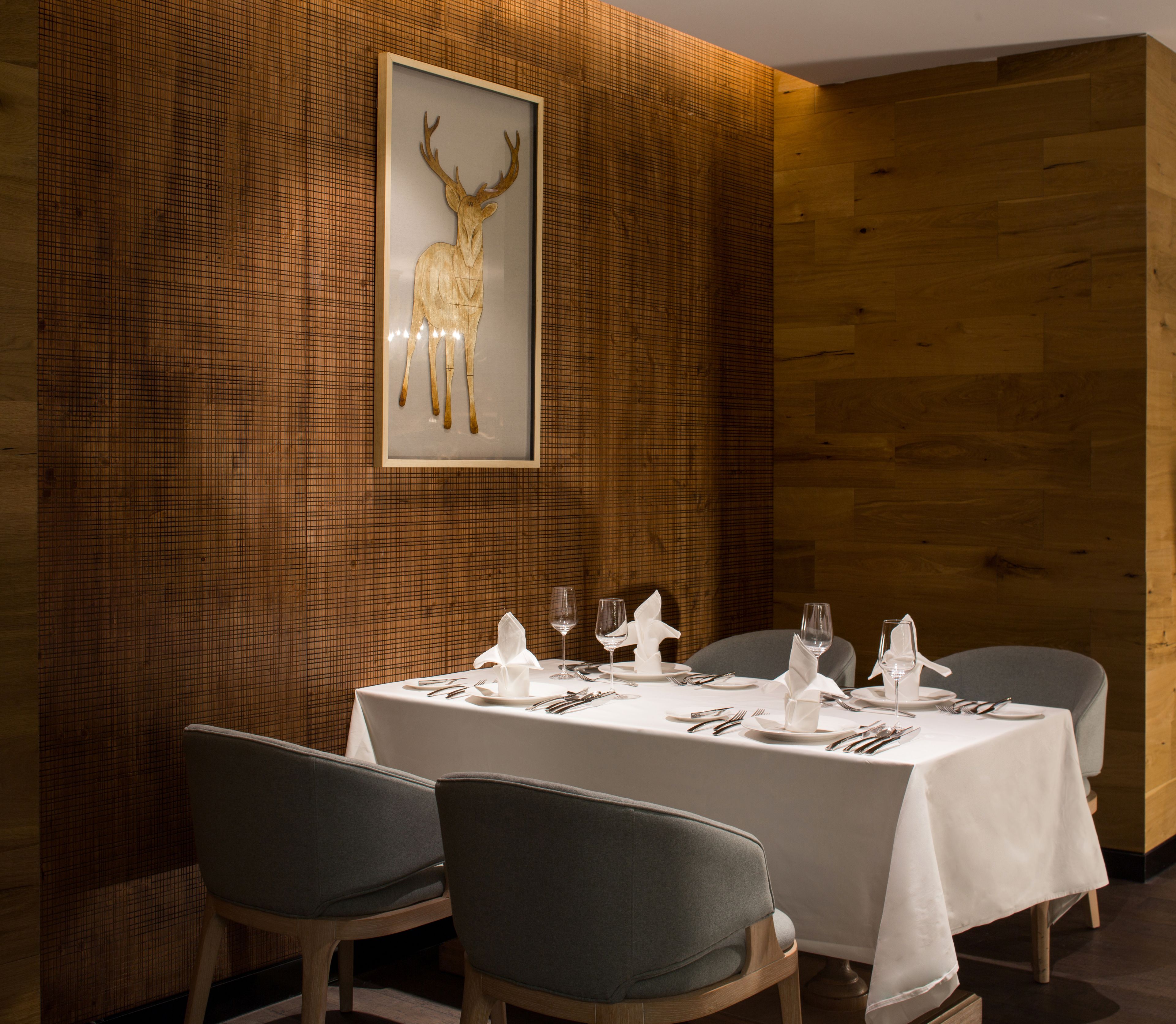 A dining area with a table set for four, chairs, and a framed deer artwork on the wall.