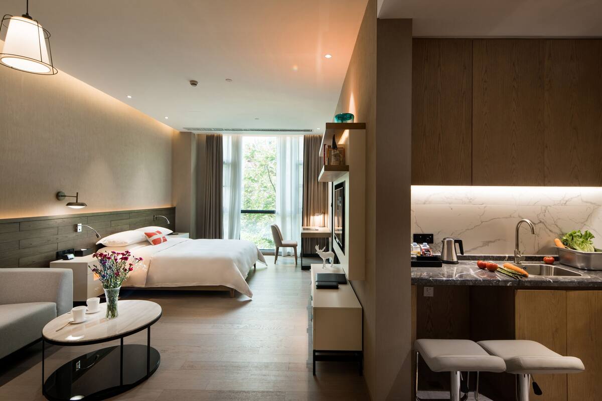 Ein modernes Hotelzimmer mit Bett, Sofa und einer kleinen Küchenzeile mit Spüle und Arbeitsplatte.