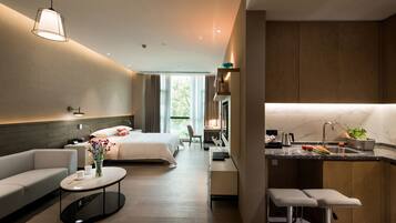 A modern hotel room with a bed, sofa, and a small kitchen area with a sink and countertop.
