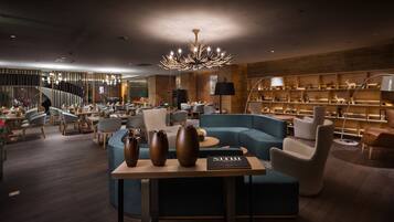 A modern lounge area with a blue sofa, a wooden table with vases, and a chandelier.