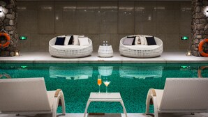 Un espace aménagé au bord de la piscine, avec deux fauteuils de relaxation en osier, une petite table avec des boissons et un mur en pierre en arrière-plan.