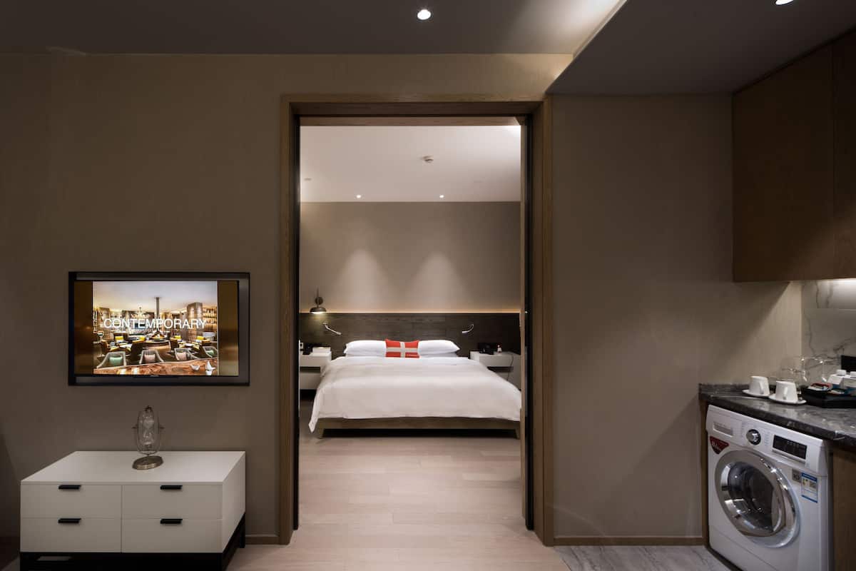 Ein modernes Hotelzimmer mit einem ordentlich bezogenen Bett, einer Waschmaschine und einem gerahmten Bild an der Wand.