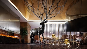 Un hall d’entrée agrémenté d’une grande sculpture métallique représentant un cerf, d’un mur en verre et d’un escalier moderne.