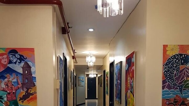 A hallway with artwork on the walls, a chandelier, and a tiled floor. - City Corner Hotel (Legazpi)
