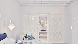 A modern bedroom with a bed, bedside table, and a view into a bathroom. - Katikies Mykonos - The Leading Hotels Of The World (Mykonos)