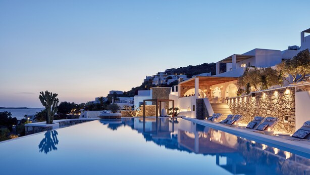 A poolside area with lounge chairs, a stone wall, and a building with a stone facade. - Katikies Mykonos - The Leading Hotels Of The World (Mykonos)