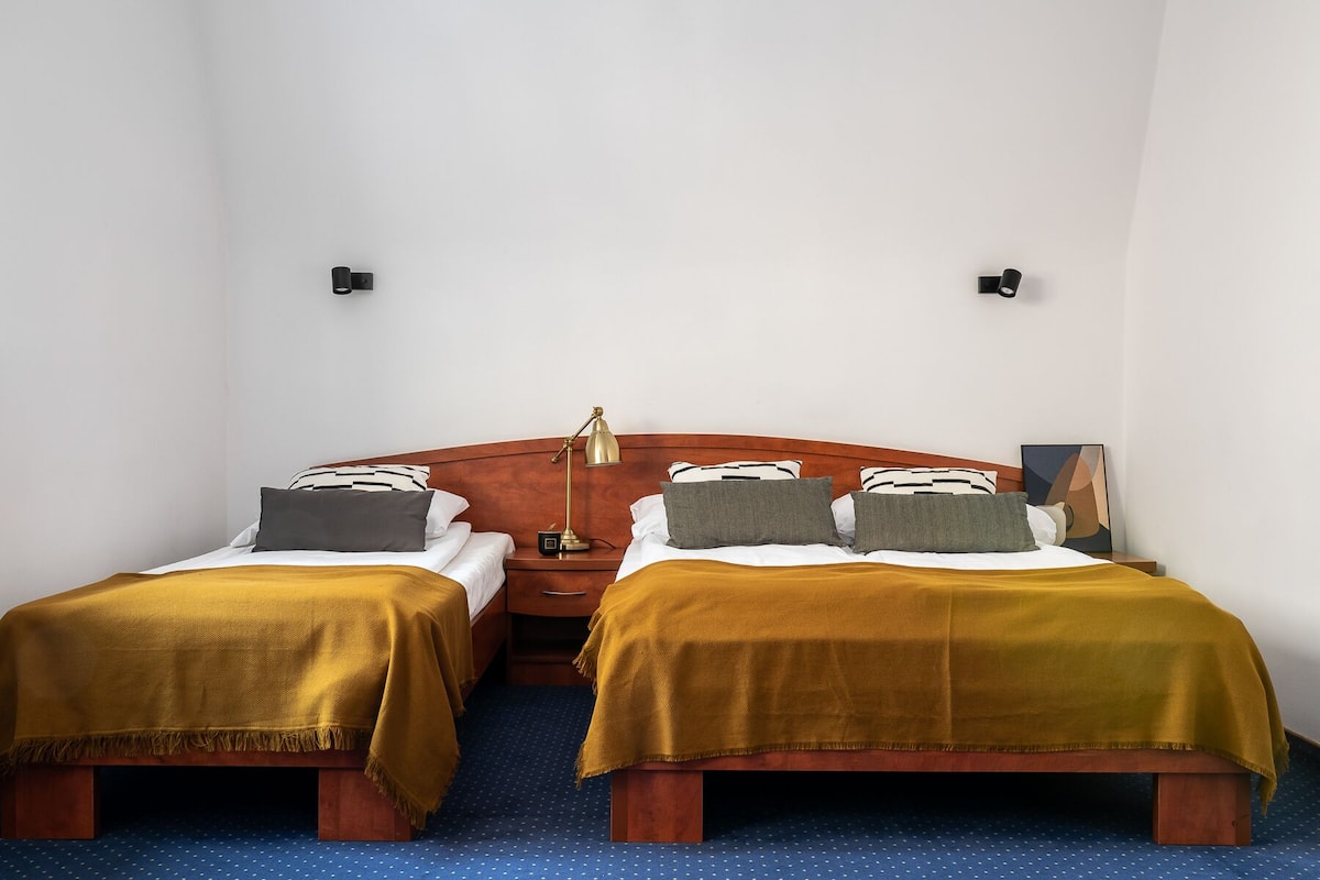 A hotel room with two beds, a wooden headboard, a nightstand with a lamp, and a small painting on the wall.