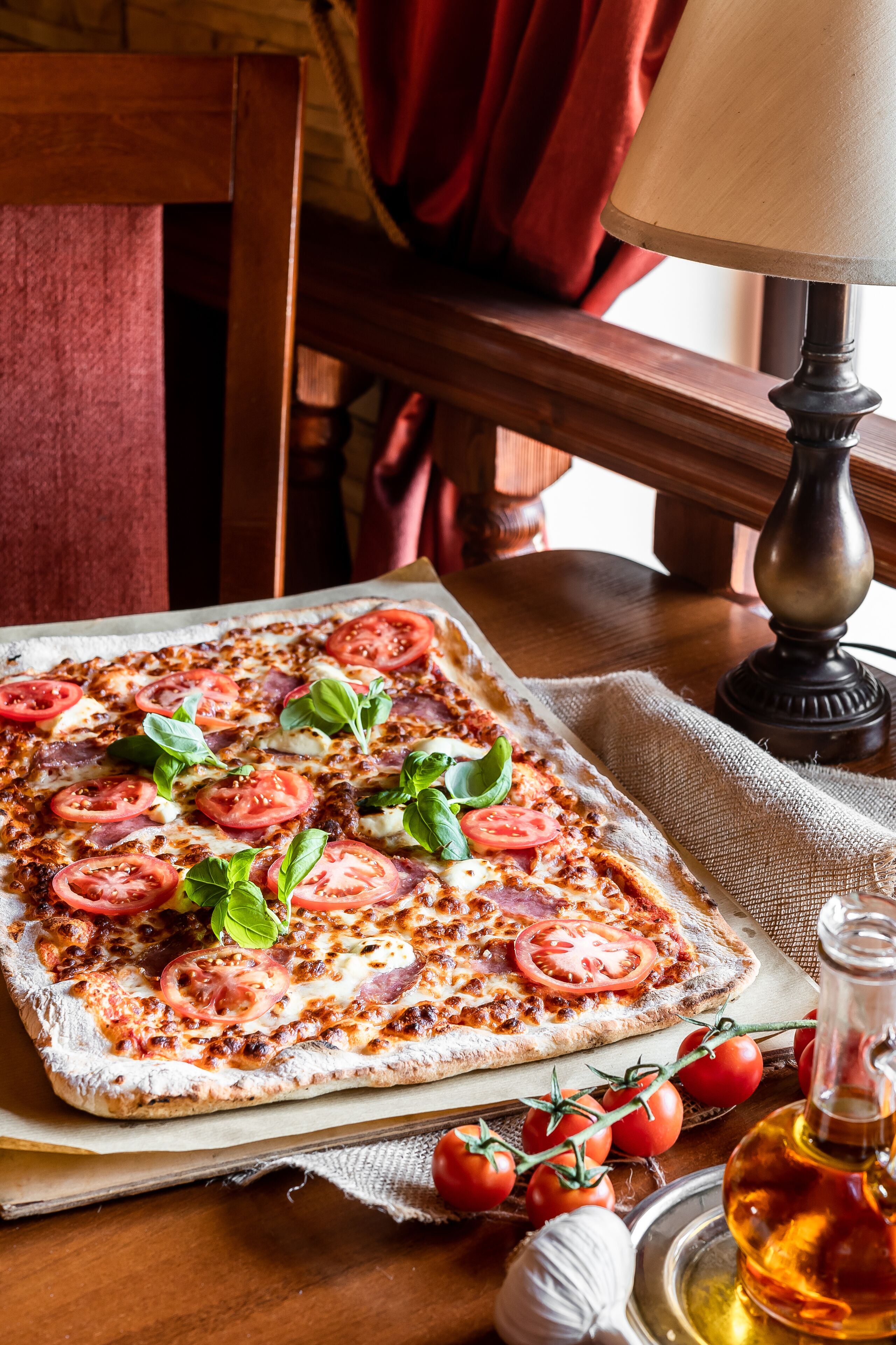 A rectangular pizza with tomato slices and basil on a wooden table.