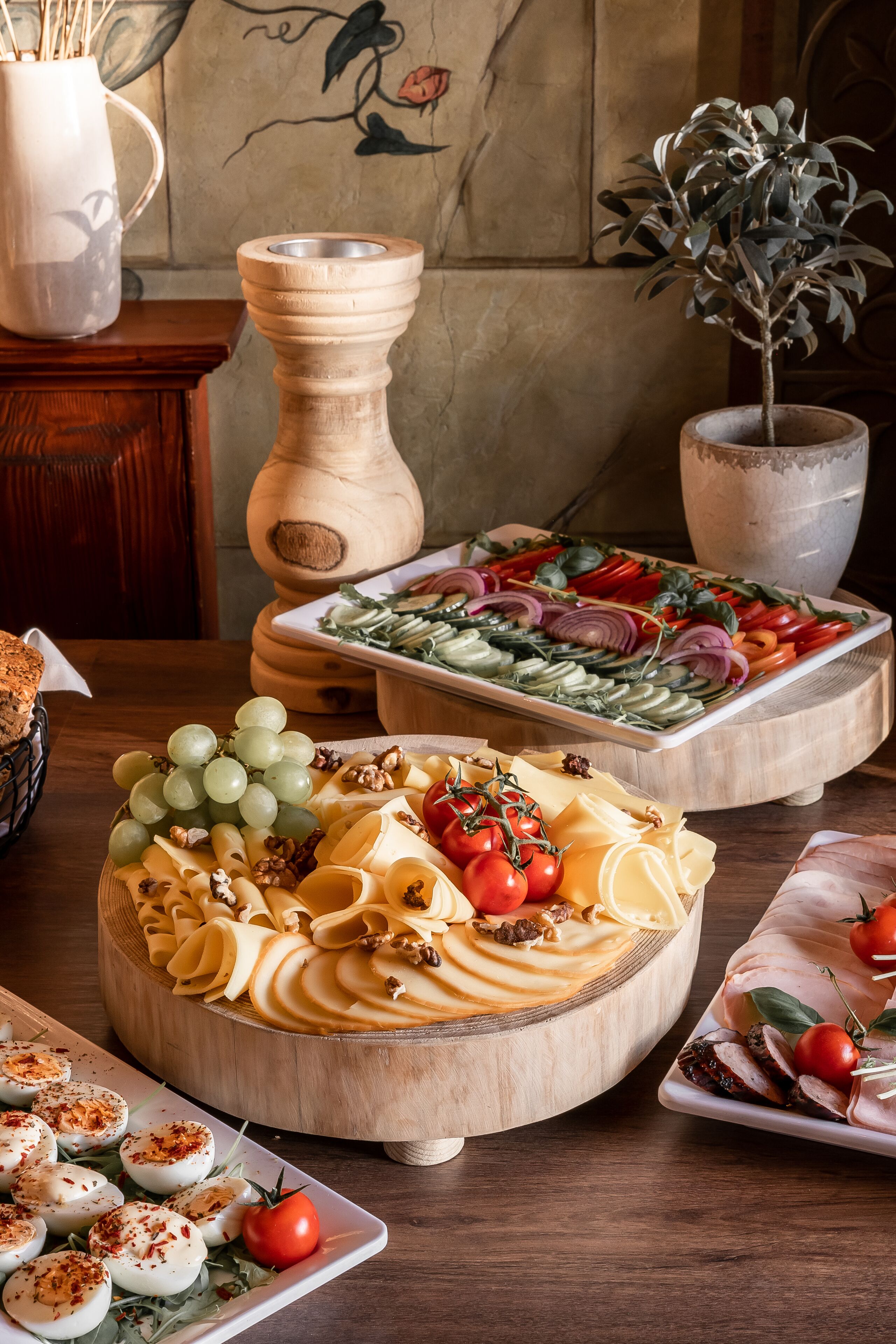 Een houten tafel met verschillende schalen vol eten, zoals druiven, kaas, tomaten en vlees.