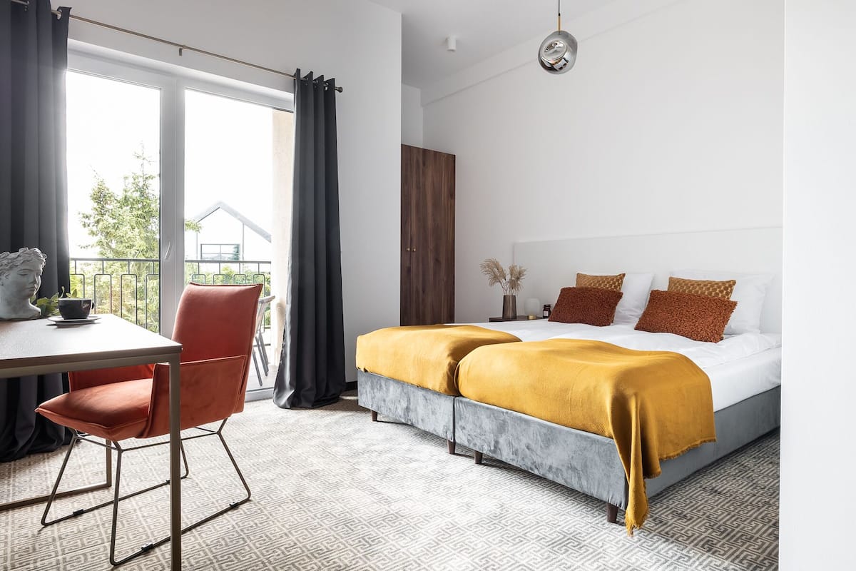 A modern hotel room with a large bed, a dining table, and a view of the outdoors.