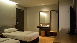 A hotel room with two beds, a wooden floor, a large mirror, a sink, and a television.