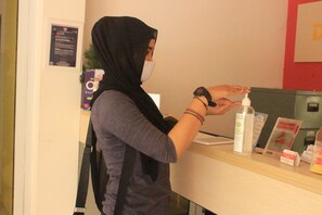 A person at a reception desk with a hand sanitizer dispenser, a framed certificate, and a small box on the counter.