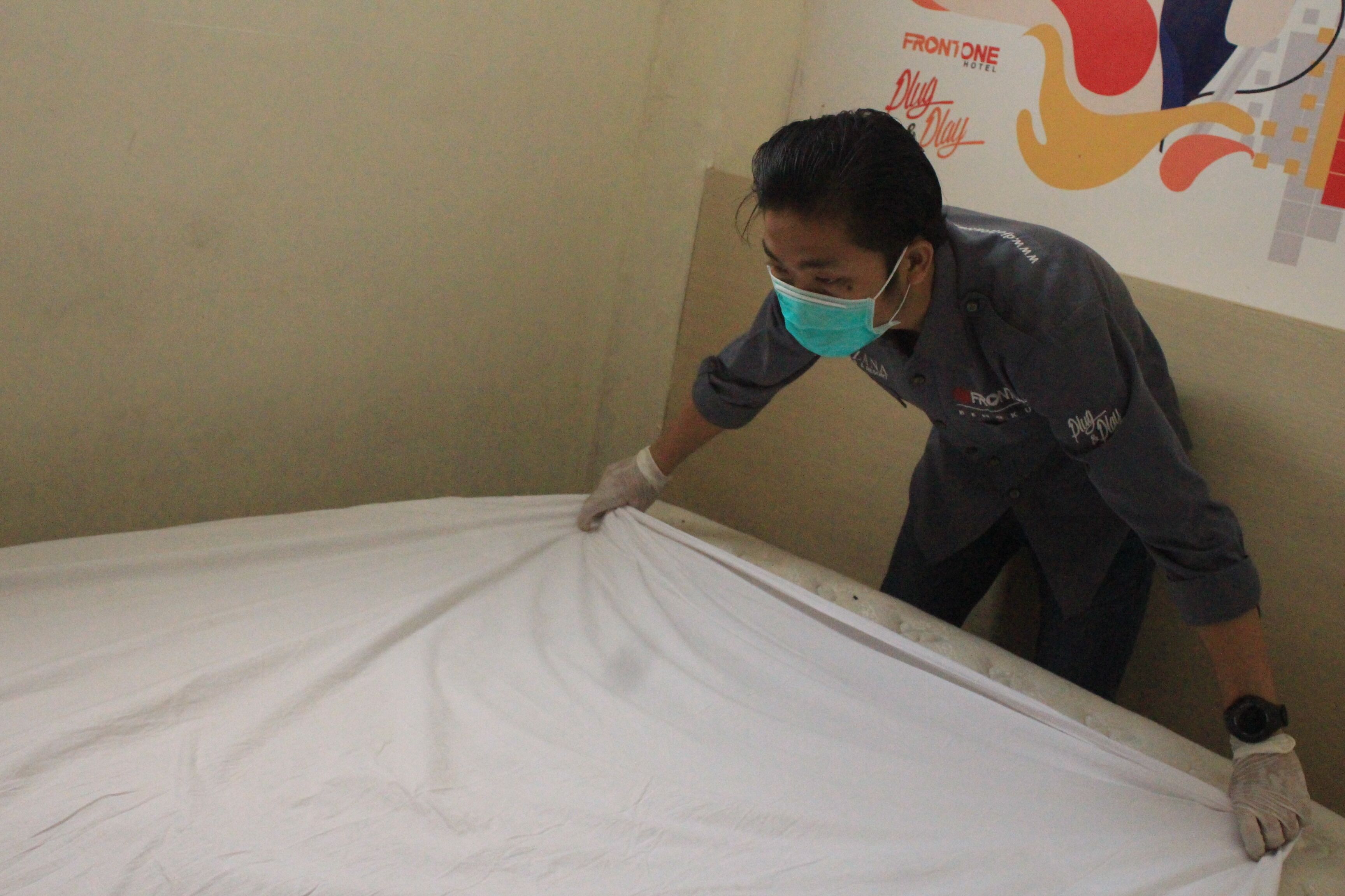 A person adjusting a bed in a room with a plain wall and a colorful poster.