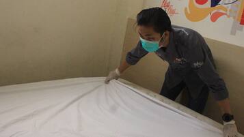 A person adjusting a bed in a room with a plain wall and a colorful poster.