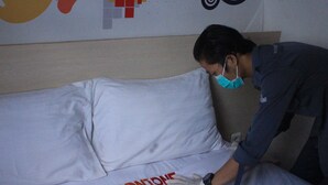 A person in a dark uniform adjusting a white bed with red text. - Djo Front One Inn Bengkulu (Bengkulu)