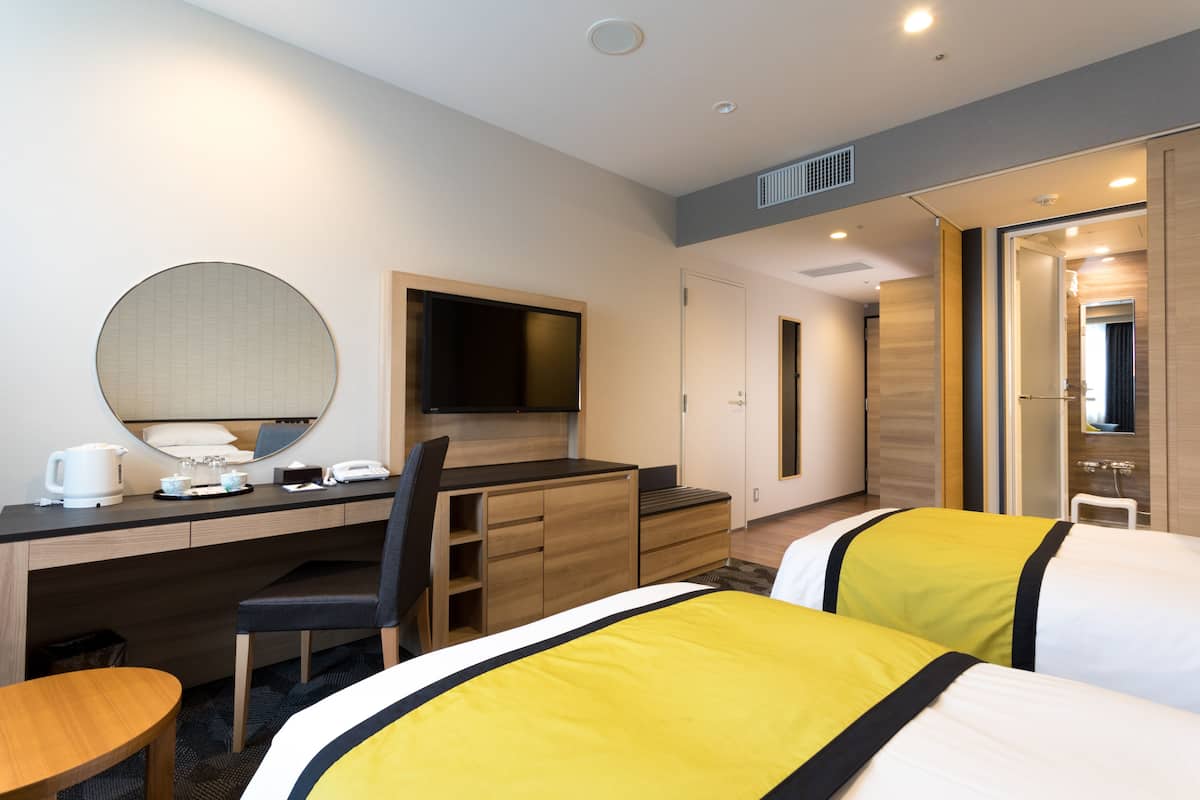 A hotel room with a desk, chair, bed, and a television.