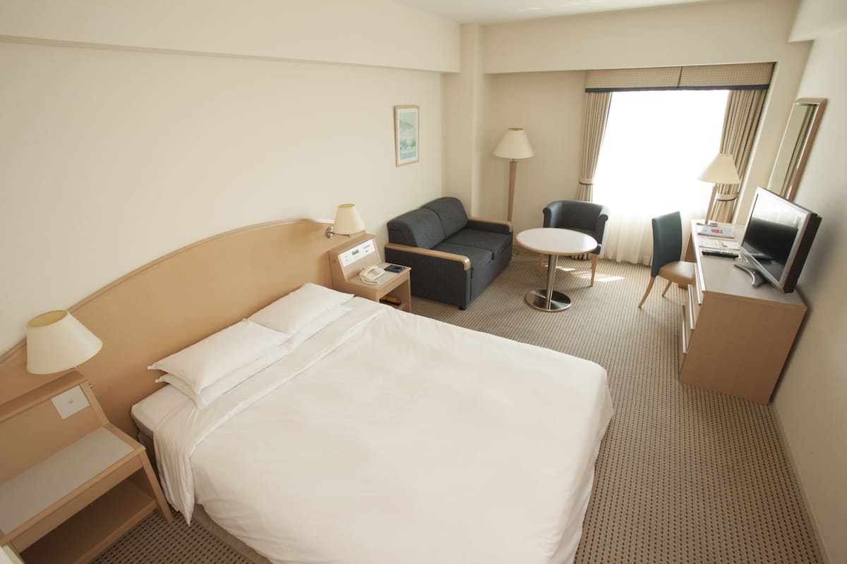 A hotel room with a large bed, a sofa, a desk with a computer, a chair, and a small table.