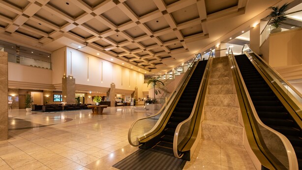 A spacious lobby with two escalators, a reception area, and a high ceiling with a grid pattern. - Hotel Hewitt Koshien (Nishinomiya)