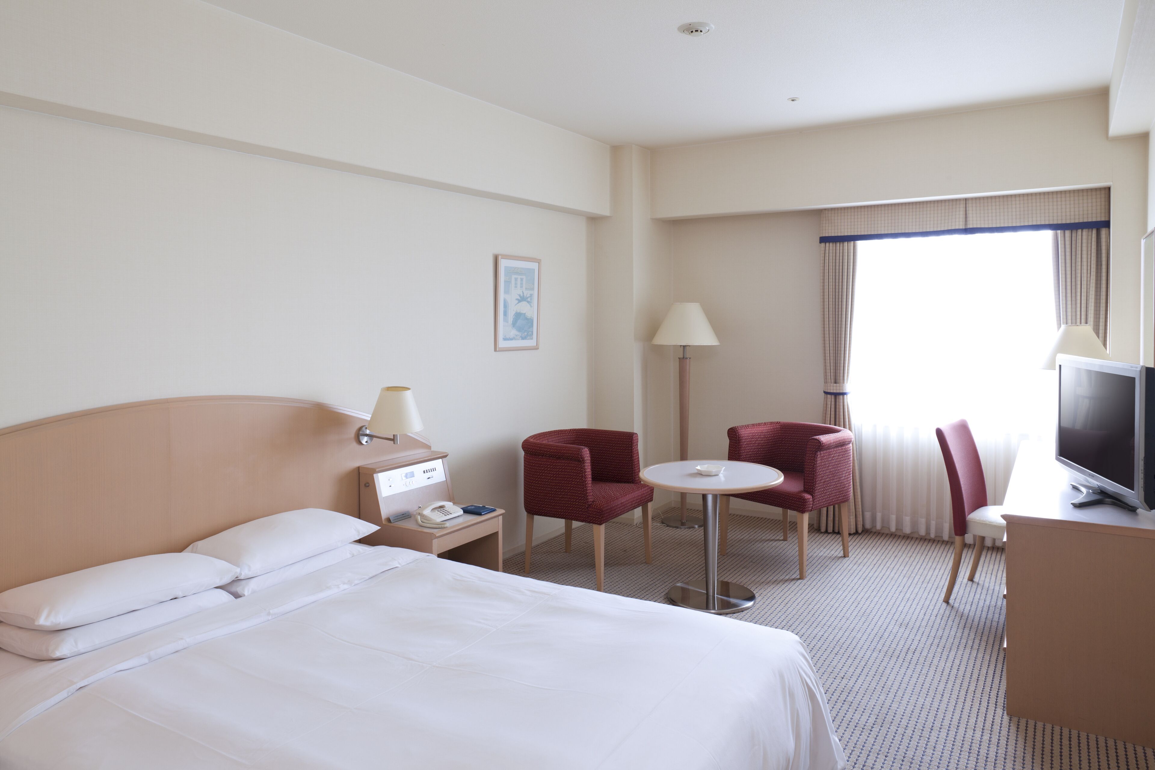 A hotel room with a bed, a desk, a TV, a lamp, and two chairs.