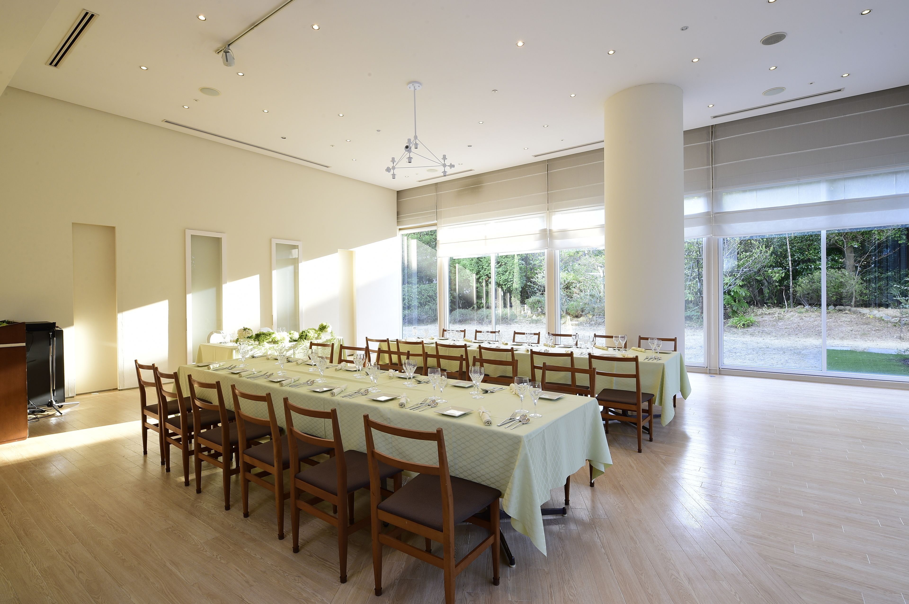 A spacious dining area with long tables set for a meal, large windows offering a view of the outdoors, and a modern ceiling design.