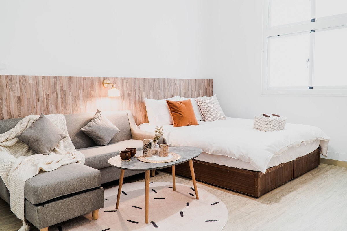 A modern bedroom with a sofa, a bed, a round table, and a nightstand.