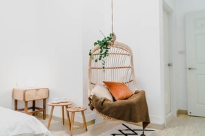 Une pièce avec un fauteuil suspendu, une petite table avec des tasses et un tabouret en rotin.