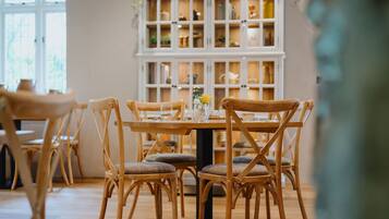 A dining area with wooden chairs and a table, a white cabinet with glass doors in the background, and a vase with flowers on the table.