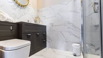 A bathroom with a toilet, dark wooden cabinet, marble tiles, and a glass shower enclosure.