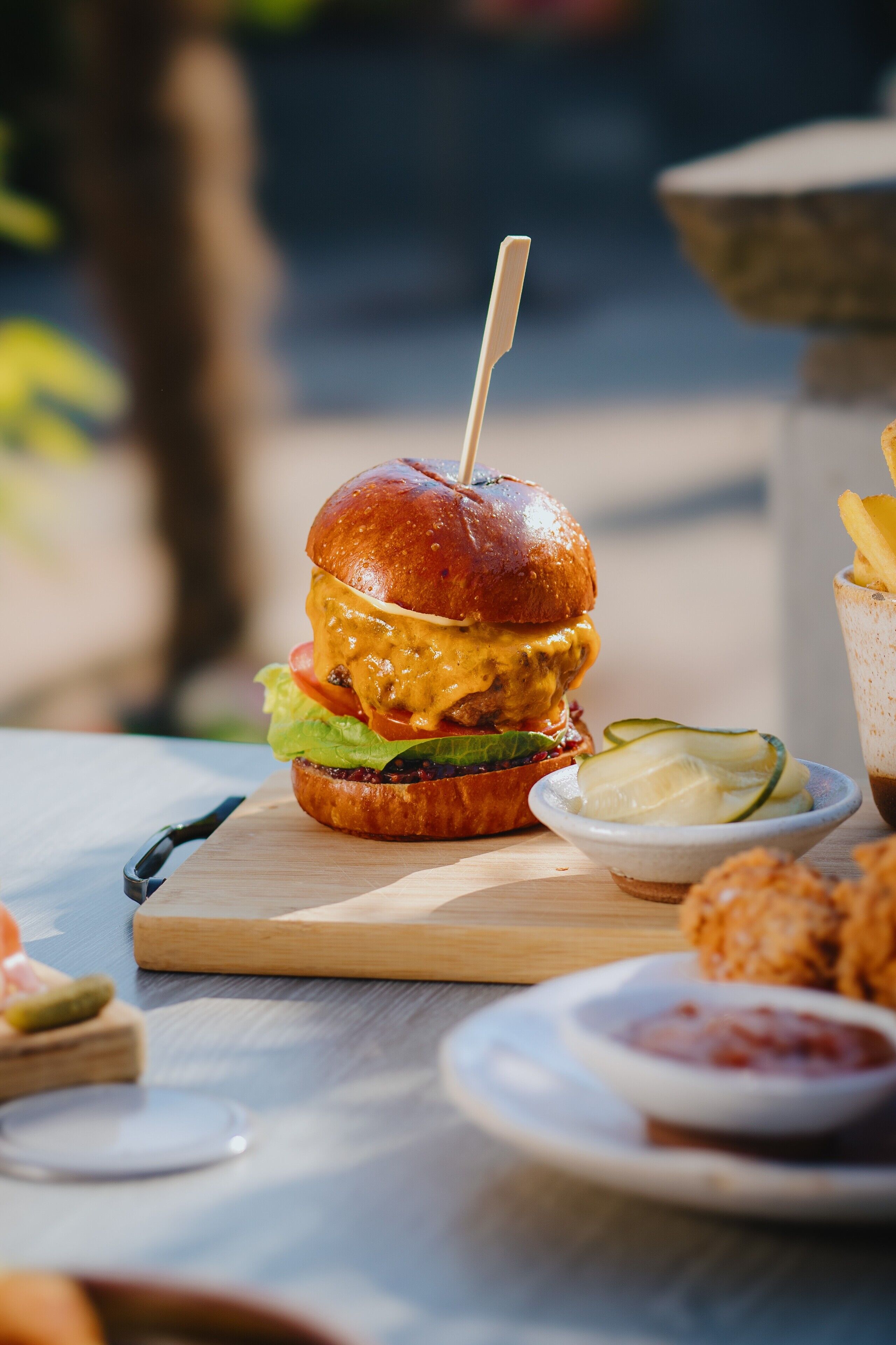 A burger with a toothpick, lettuce, tomato, and cheese on a wooden board.