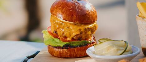 A burger with a toothpick, lettuce, tomato, and cheese on a wooden board.
