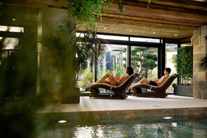 Two lounge chairs by an indoor pool with a view of greenery and a stone wall. - Lanelay Hall Hotel & Spa (Pontyclun)