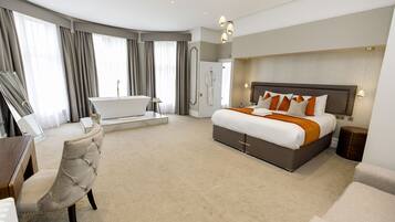 A modern hotel room with a large bed, a sitting area with a chair, a bathtub, and a large window with curtains.