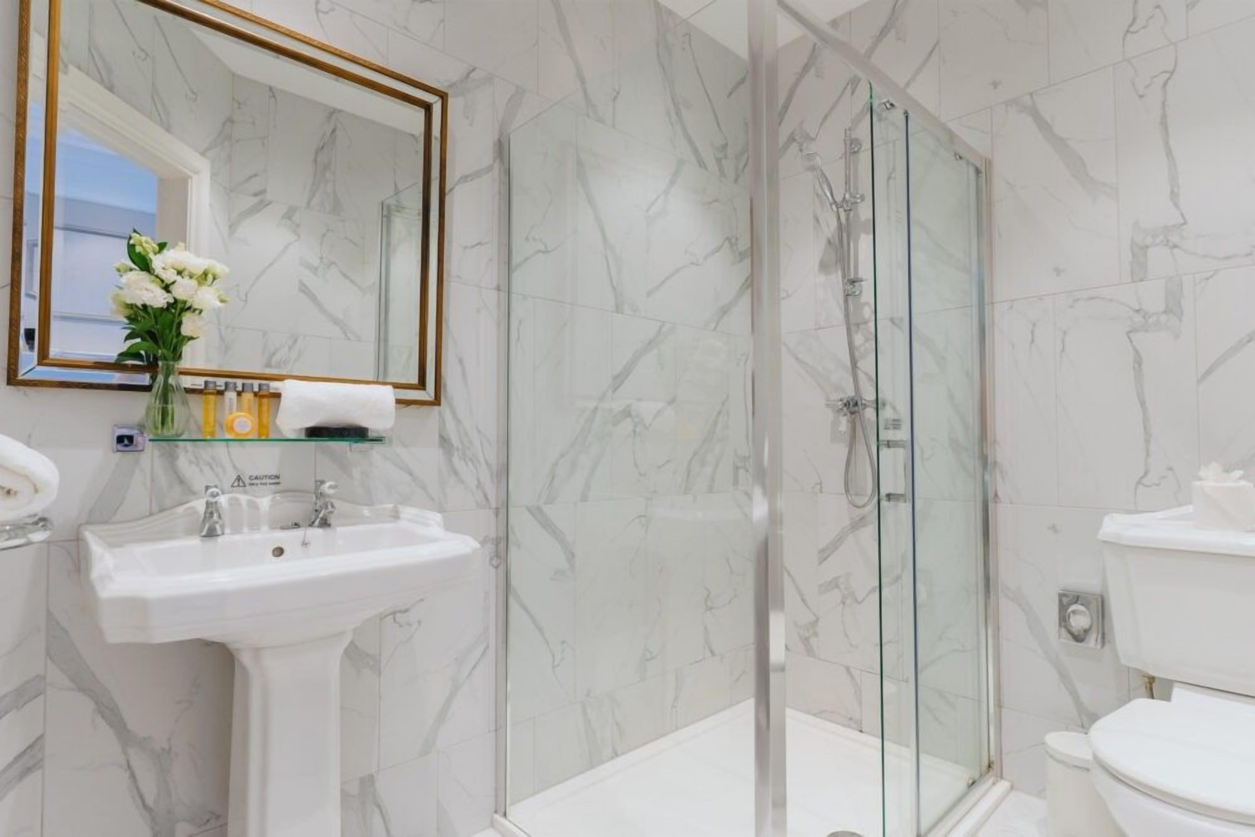 A bathroom with a marble wall, a glass shower enclosure, a sink, and a toilet.